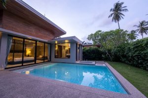 Piscine moderne avec terrasse en béton dans une maison contemporaine entourée de verdure.